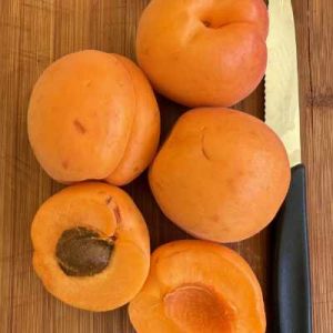 Whole and half apricots with knife on wooden board